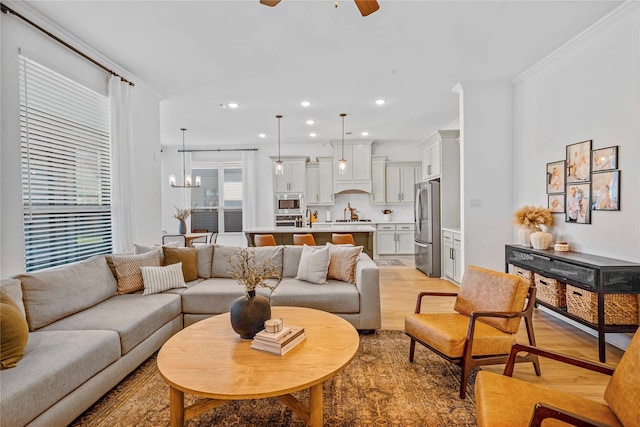 living area featuring recessed lighting, ceiling fan with notable chandelier, crown molding, and light wood-style floors