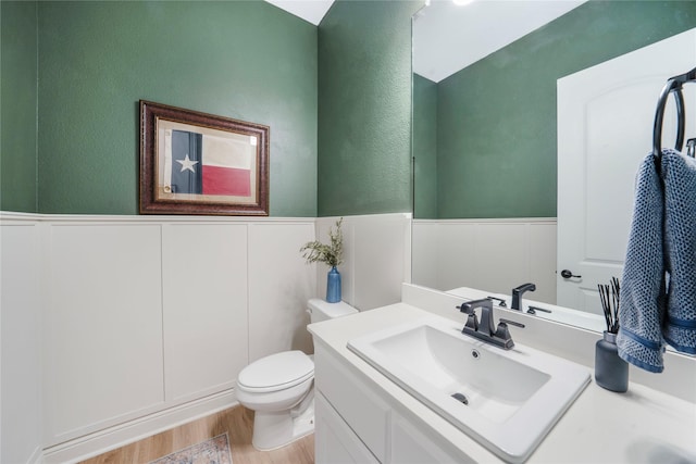 bathroom with vanity, toilet, wood finished floors, and wainscoting