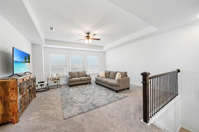 carpeted living area with a raised ceiling, a ceiling fan, visible vents, and baseboards