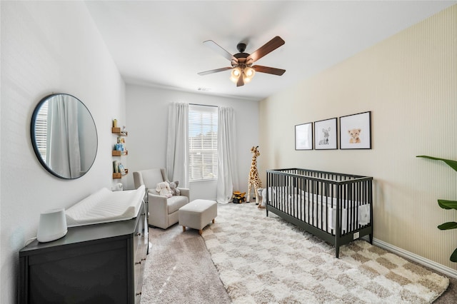 carpeted bedroom with baseboards, a nursery area, and ceiling fan