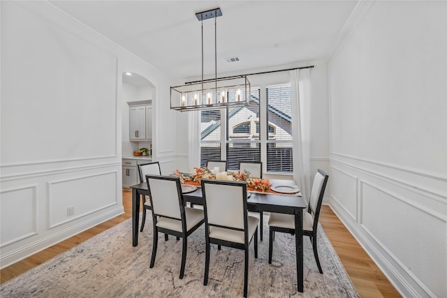 dining area featuring visible vents, crown molding, a chandelier, light wood-type flooring, and a decorative wall