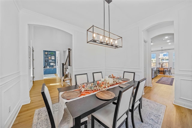 dining area featuring arched walkways, ornamental molding, a decorative wall, light wood-type flooring, and a chandelier