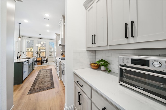 kitchen featuring visible vents, stainless steel dishwasher, light wood-style flooring, and light countertops