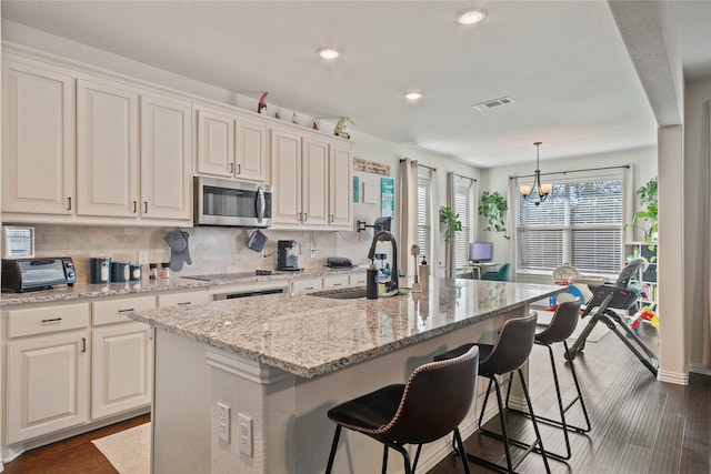 kitchen featuring sink, an island with sink, hanging light fixtures, and white cabinets