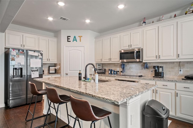 kitchen with a kitchen breakfast bar, stainless steel appliances, an island with sink, and white cabinets