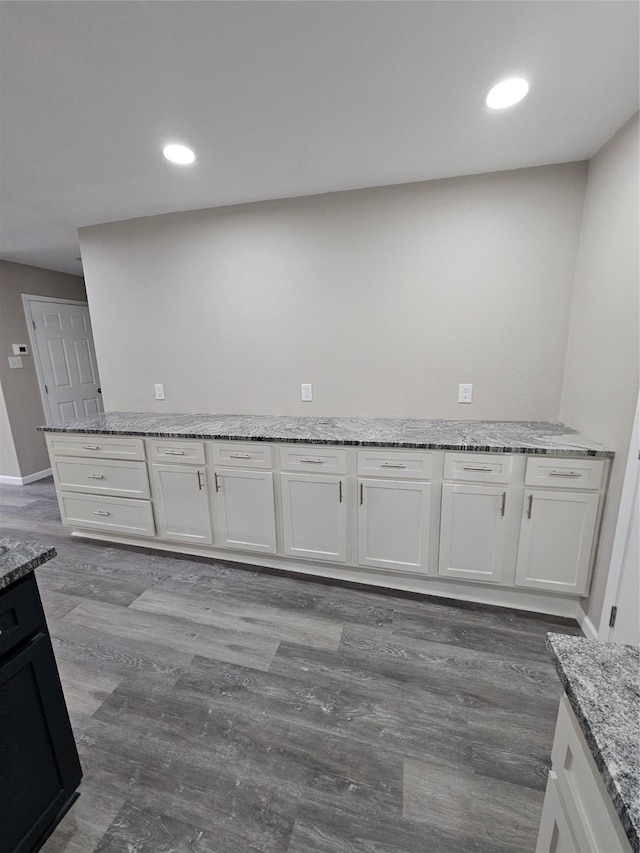 kitchen with white cabinetry, light stone counters, and wood-type flooring