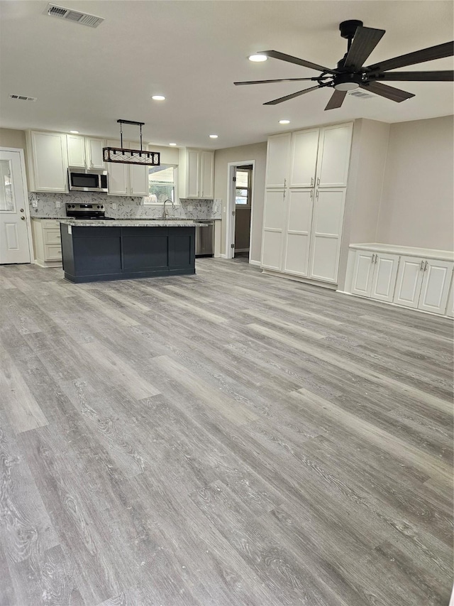 kitchen featuring stainless steel appliances, decorative light fixtures, a center island with sink, white cabinets, and light hardwood / wood-style floors