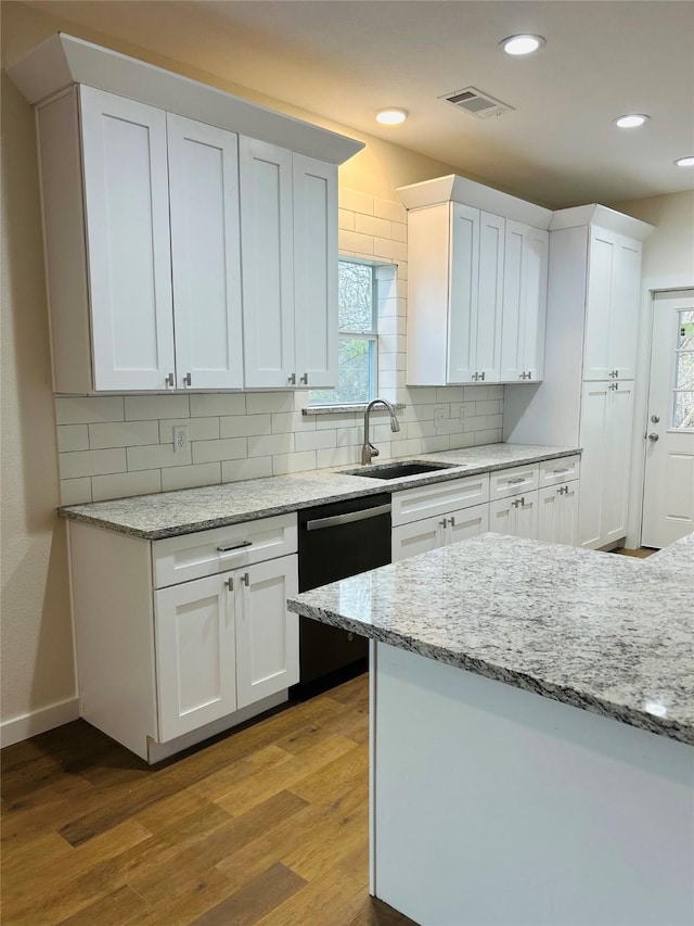 kitchen featuring white cabinetry, black dishwasher, light hardwood / wood-style floors, and light stone countertops