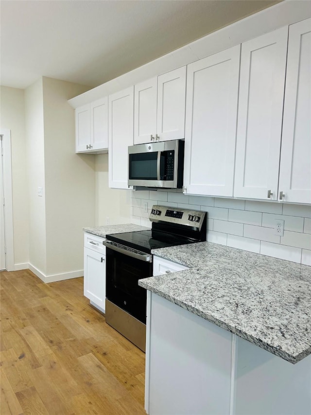 kitchen with stainless steel appliances, white cabinetry, backsplash, and light hardwood / wood-style flooring