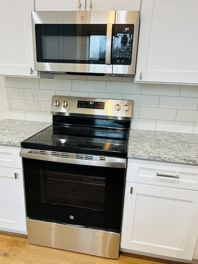 kitchen featuring backsplash, stainless steel appliances, light stone counters, light hardwood / wood-style floors, and white cabinets