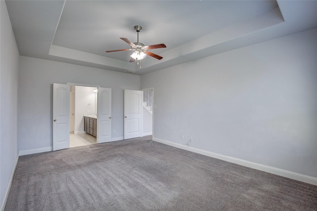 unfurnished bedroom featuring a raised ceiling, ceiling fan, light carpet, and ensuite bath