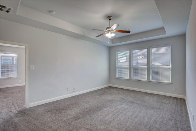 unfurnished room with a raised ceiling, ceiling fan, and carpet