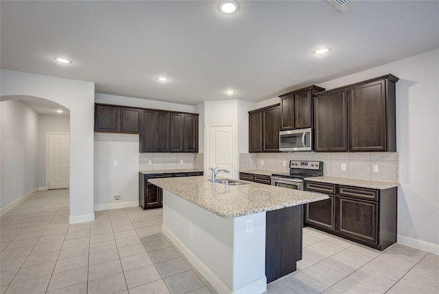 kitchen featuring appliances with stainless steel finishes, sink, backsplash, a kitchen island with sink, and light tile patterned floors