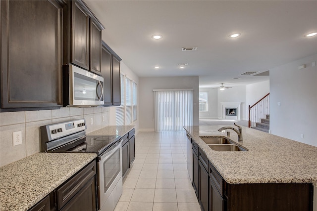 kitchen with sink, decorative backsplash, light tile patterned floors, stainless steel appliances, and a center island with sink