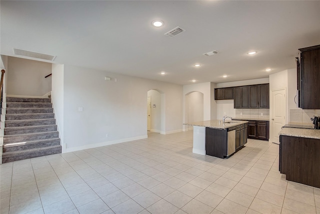 kitchen with sink, tasteful backsplash, light stone counters, a center island with sink, and light tile patterned floors