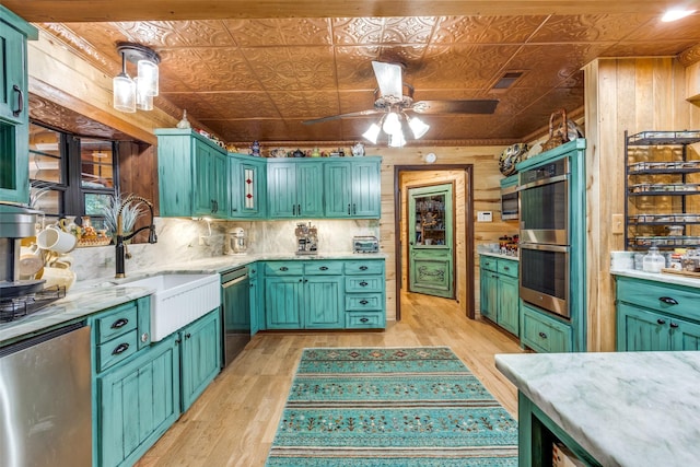 kitchen with sink, light hardwood / wood-style flooring, pendant lighting, wooden walls, and appliances with stainless steel finishes