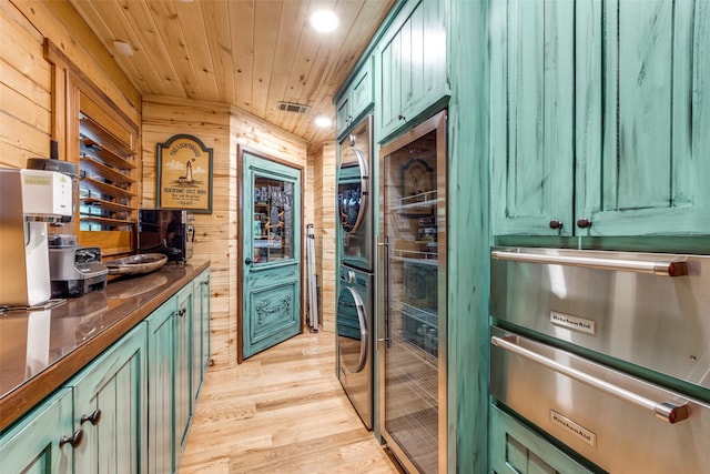 kitchen with wood walls, green cabinets, light wood-type flooring, and stacked washer and clothes dryer