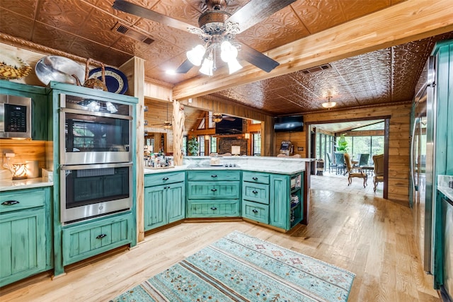 kitchen with kitchen peninsula, light wood-type flooring, stainless steel appliances, wooden walls, and green cabinetry