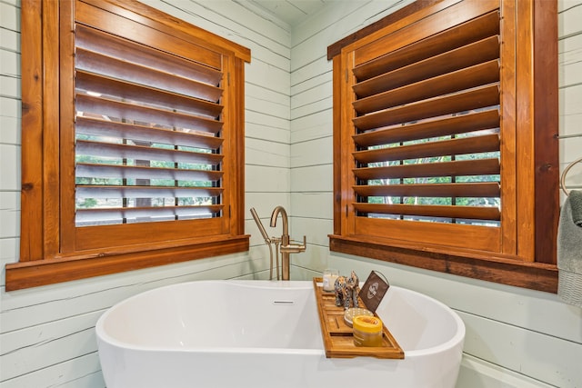 bathroom featuring a tub to relax in, a wealth of natural light, and wooden walls