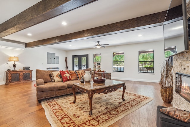 living room featuring ceiling fan, beam ceiling, a stone fireplace, and light hardwood / wood-style flooring