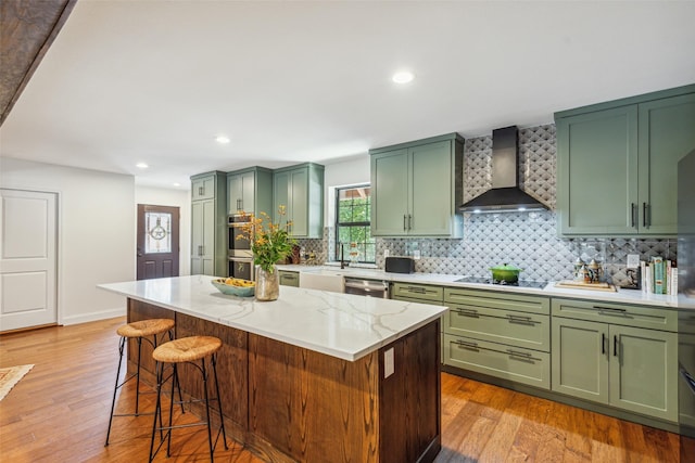 kitchen featuring light stone countertops, a center island, wall chimney exhaust hood, green cabinets, and light wood-type flooring