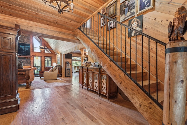 stairway with hardwood / wood-style floors, wood walls, ceiling fan with notable chandelier, vaulted ceiling, and wood ceiling