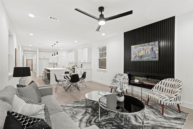 living room with ceiling fan, sink, and light wood-type flooring