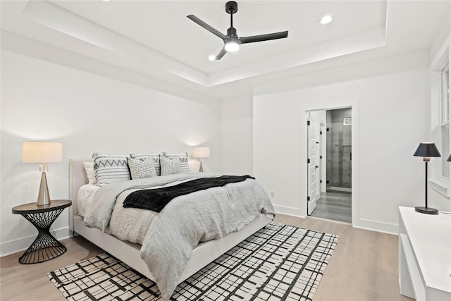 bedroom with ceiling fan, a raised ceiling, light wood-type flooring, and ensuite bathroom