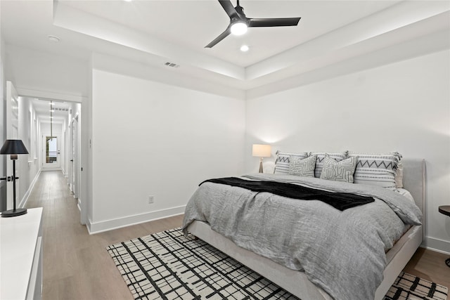 bedroom featuring ceiling fan, light wood-type flooring, and a tray ceiling