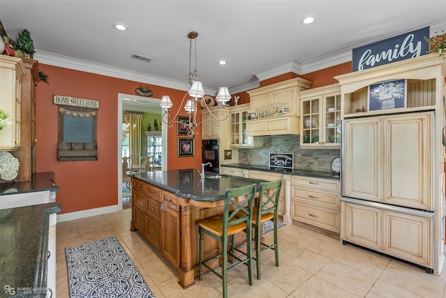 kitchen featuring a kitchen bar, hanging light fixtures, ornamental molding, an island with sink, and cream cabinetry