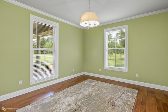 empty room featuring dark wood-type flooring, ornamental molding, plenty of natural light, and a chandelier