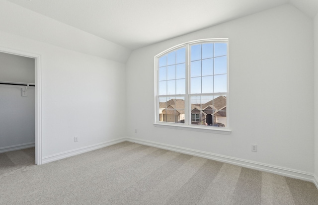 unfurnished bedroom featuring carpet floors, a spacious closet, vaulted ceiling, and a closet