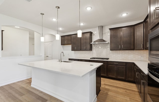 kitchen featuring appliances with stainless steel finishes, decorative light fixtures, an island with sink, sink, and wall chimney range hood