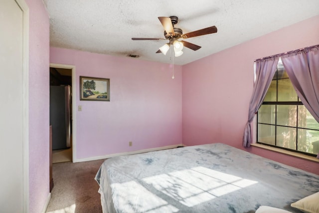 carpeted bedroom with ceiling fan, a textured ceiling, and stainless steel refrigerator