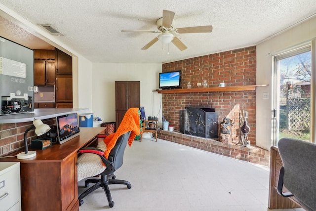 home office with a textured ceiling, a brick fireplace, and ceiling fan