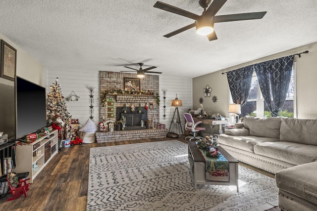 living room featuring a brick fireplace, dark wood-type flooring, a textured ceiling, and ceiling fan