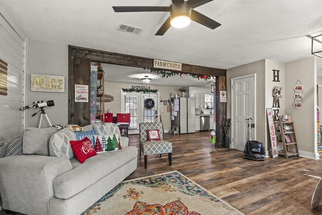 living room with dark wood-type flooring, ceiling fan, and a textured ceiling