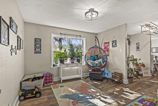 recreation room with dark wood-type flooring, a notable chandelier, and a textured ceiling