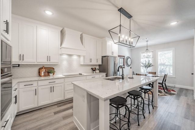 kitchen featuring premium range hood, stainless steel appliances, sink, a center island with sink, and white cabinets