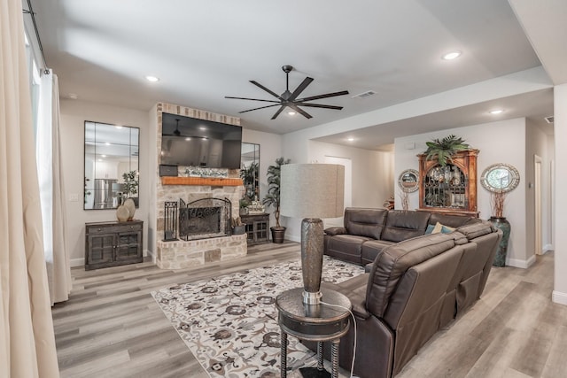 living room with ceiling fan, light hardwood / wood-style floors, and a stone fireplace