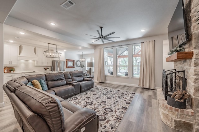 living room featuring ceiling fan with notable chandelier, light hardwood / wood-style floors, and a stone fireplace