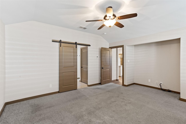 unfurnished bedroom featuring vaulted ceiling, a barn door, light carpet, and ceiling fan