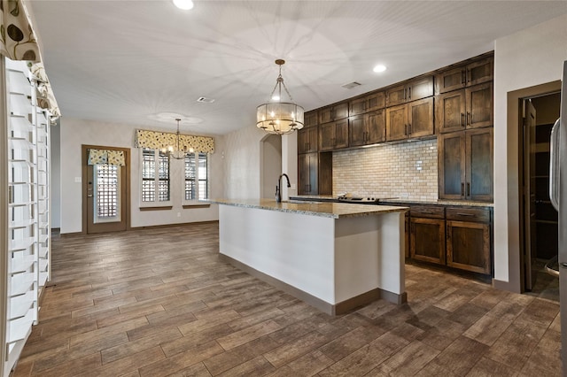 kitchen with dark brown cabinetry, light stone counters, decorative light fixtures, a chandelier, and a center island with sink