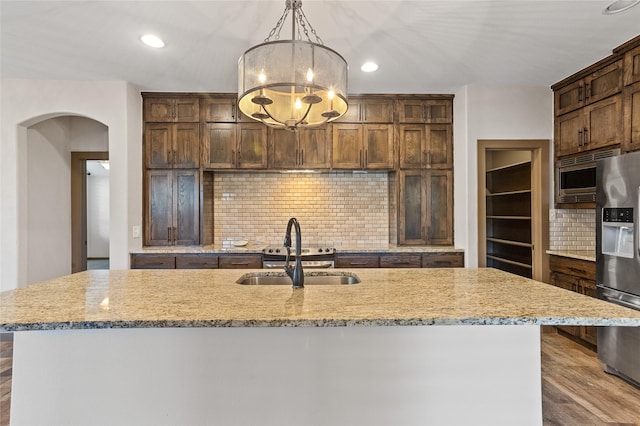 kitchen featuring sink, hanging light fixtures, stainless steel appliances, light stone countertops, and an island with sink