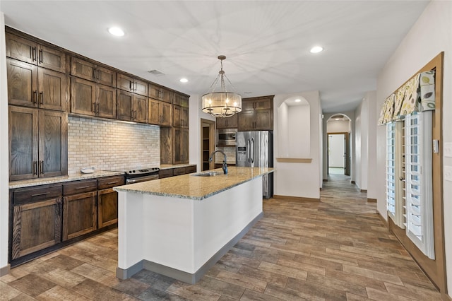 kitchen with sink, light stone counters, decorative light fixtures, a center island with sink, and stainless steel appliances