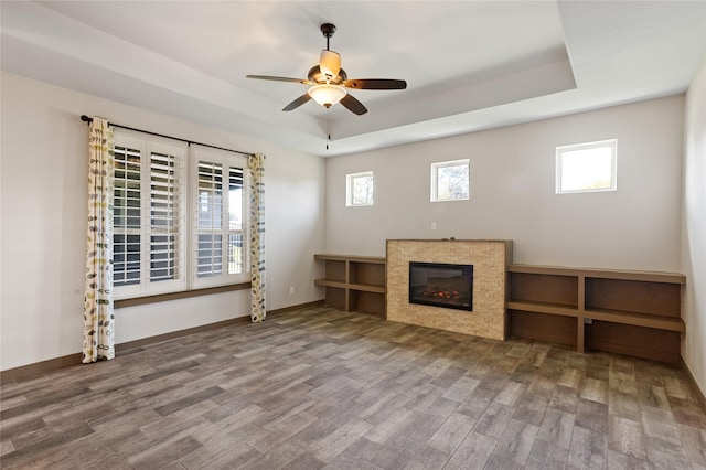 unfurnished living room with hardwood / wood-style floors, a tray ceiling, and a healthy amount of sunlight