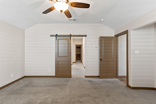 unfurnished bedroom featuring ceiling fan, a barn door, vaulted ceiling, and light carpet