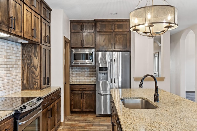 kitchen featuring appliances with stainless steel finishes, pendant lighting, sink, light stone counters, and dark wood-type flooring