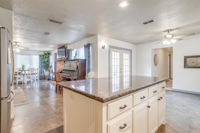 kitchen with stainless steel fridge, french doors, a textured ceiling, dark stone countertops, and a kitchen island