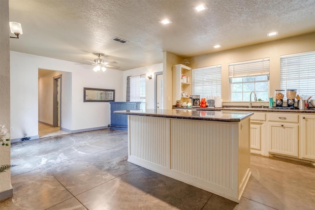 kitchen with ceiling fan, a kitchen island, dark stone countertops, and a textured ceiling